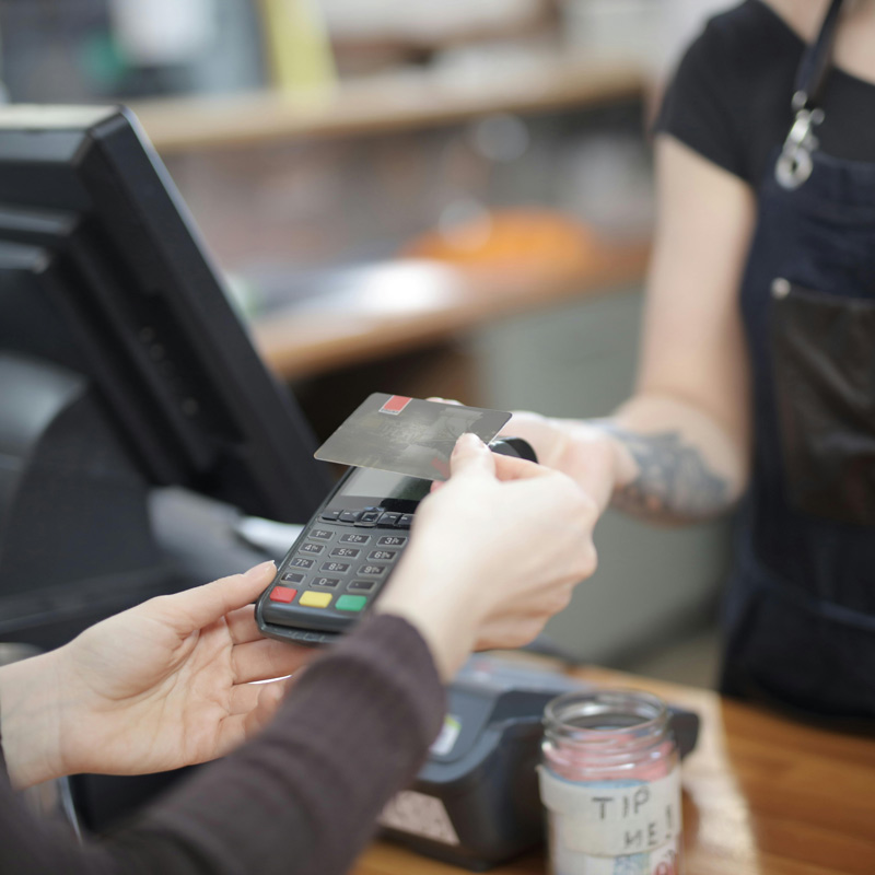 Close-up-view-of-a-customer's-hand-giving-a-credit-card-to-a-cafe-employee-at-the-cash-register,-with-a-tip-jar-visible-on-the-counter.