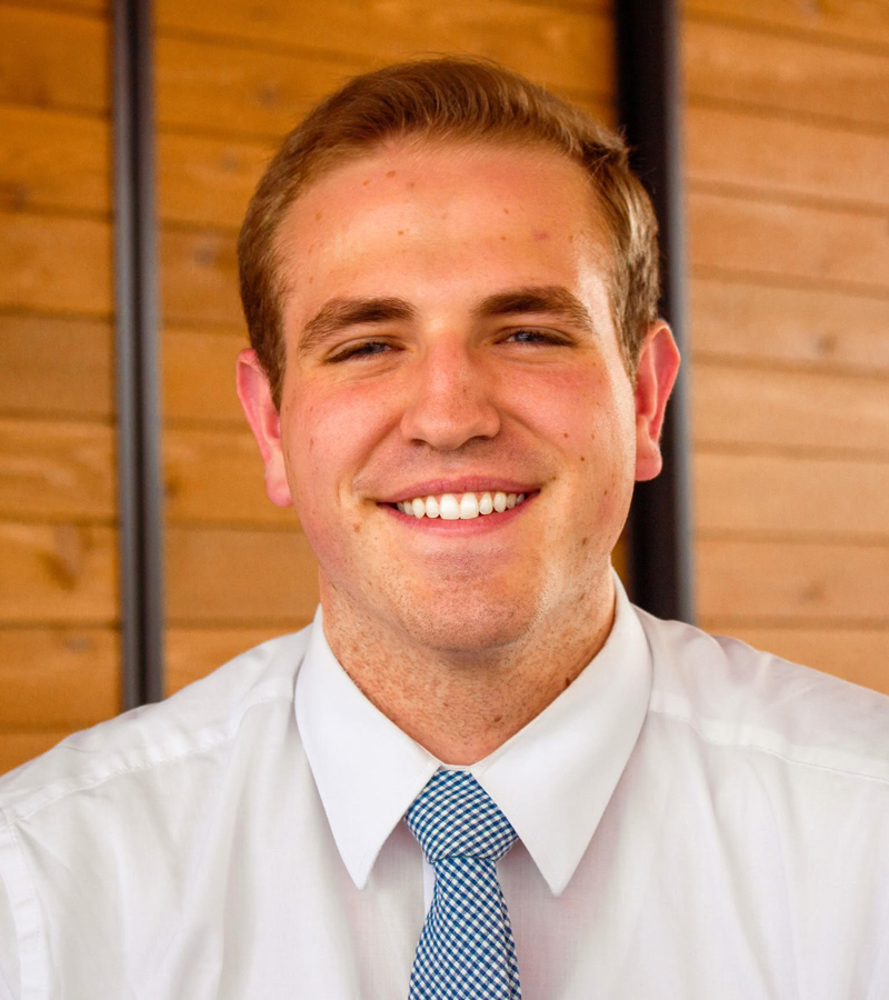 Close-up-portrait-of-a-smiling-young-man-wearing-a-white-shirt-and-a-blue-tie-against-a-wooden-background.